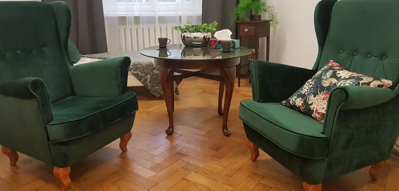 Dwa zielone fotele uszaki przy okrągłym stoliku w gabinecie