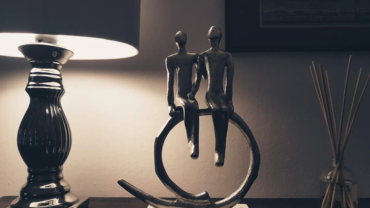 Metalowa rzeźba dwóch postaci siedzących obok siebie na kole, obok lampa