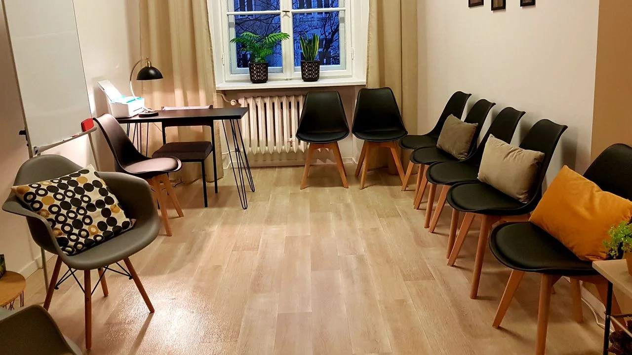 Krzesła ustawione w krąg w jasnej sali z oknem — psychoterapia grupowa